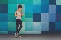 Girl standing against colorful wall with headphones looking at her phone