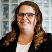 A female therapist with glasses and brunette hair wearing a black blazer and a white top